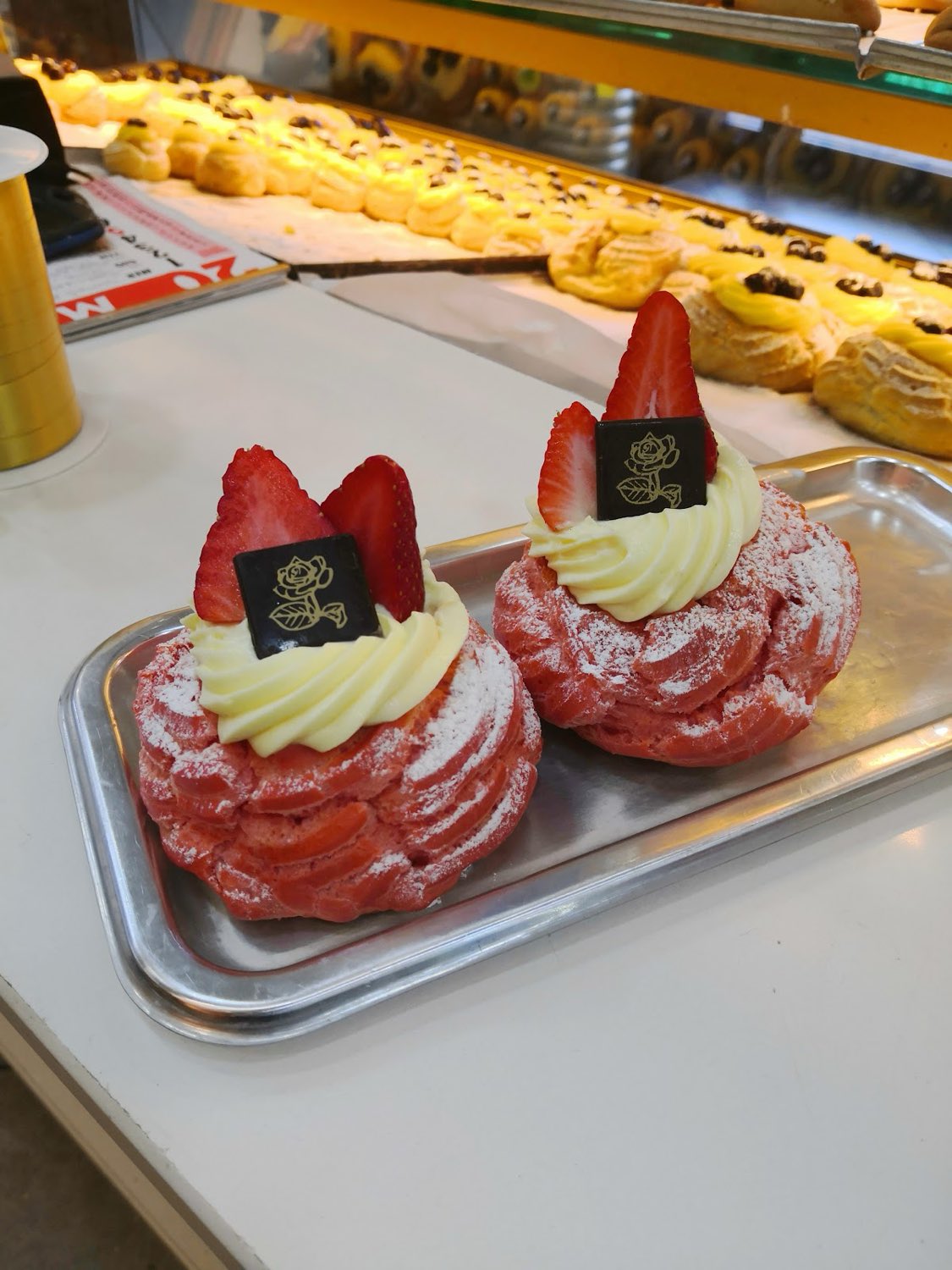 Bignè con crema montata, fragole e placchetta di cioccolato con il marchio a rosa dorata